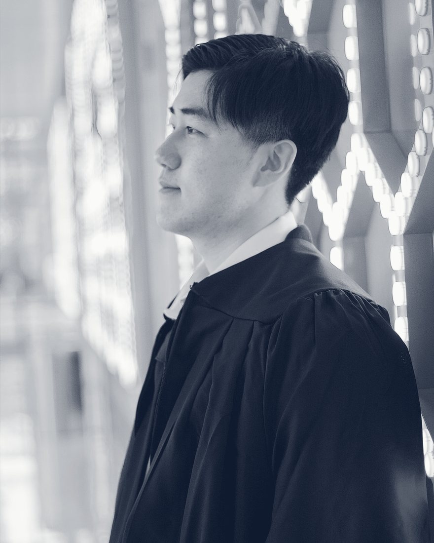 Profile portrait of a graduate in his gown, lit by a wall of colored lights