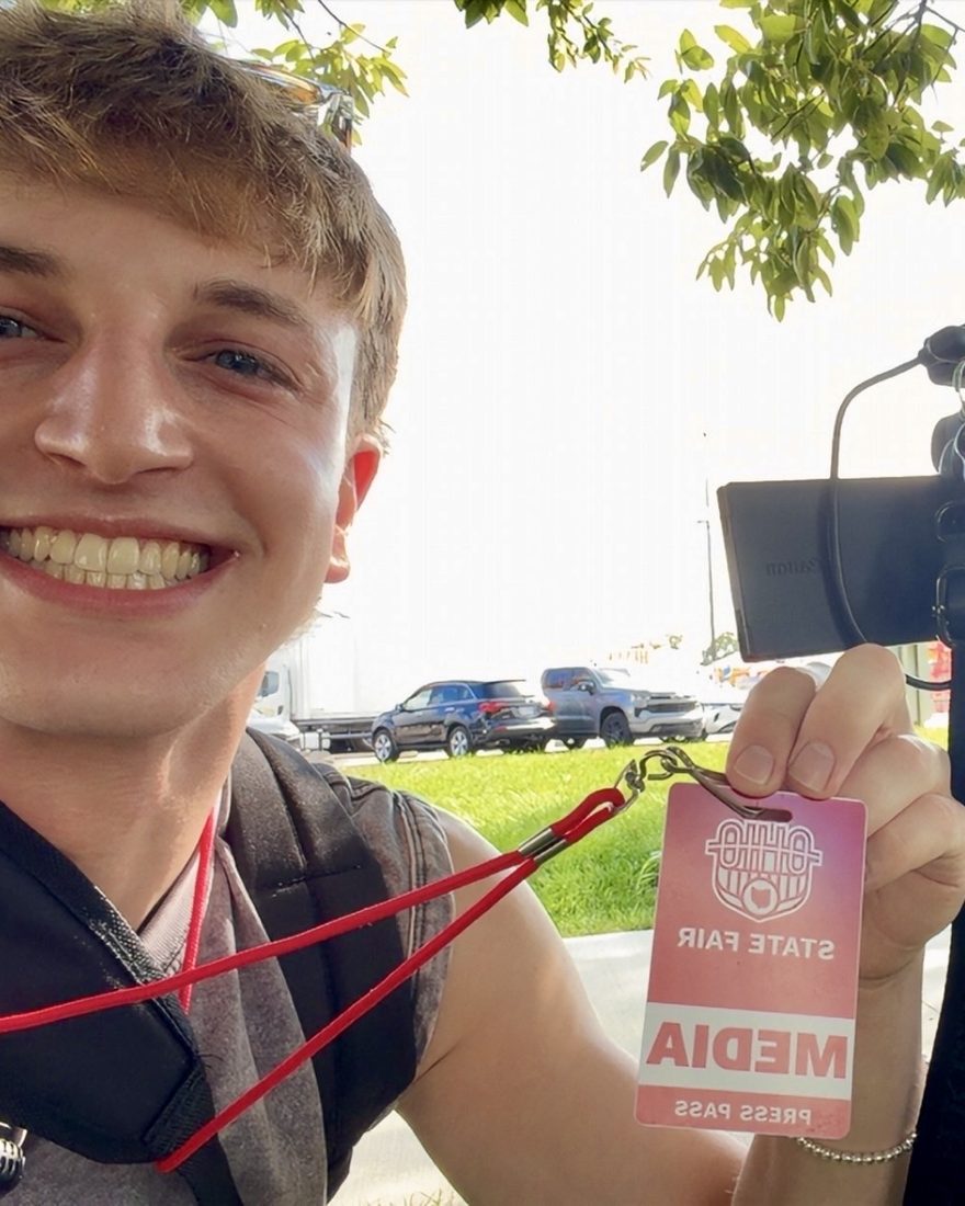 Anthony holding up an Ohio State Fair media pass beside a camera on a tripod