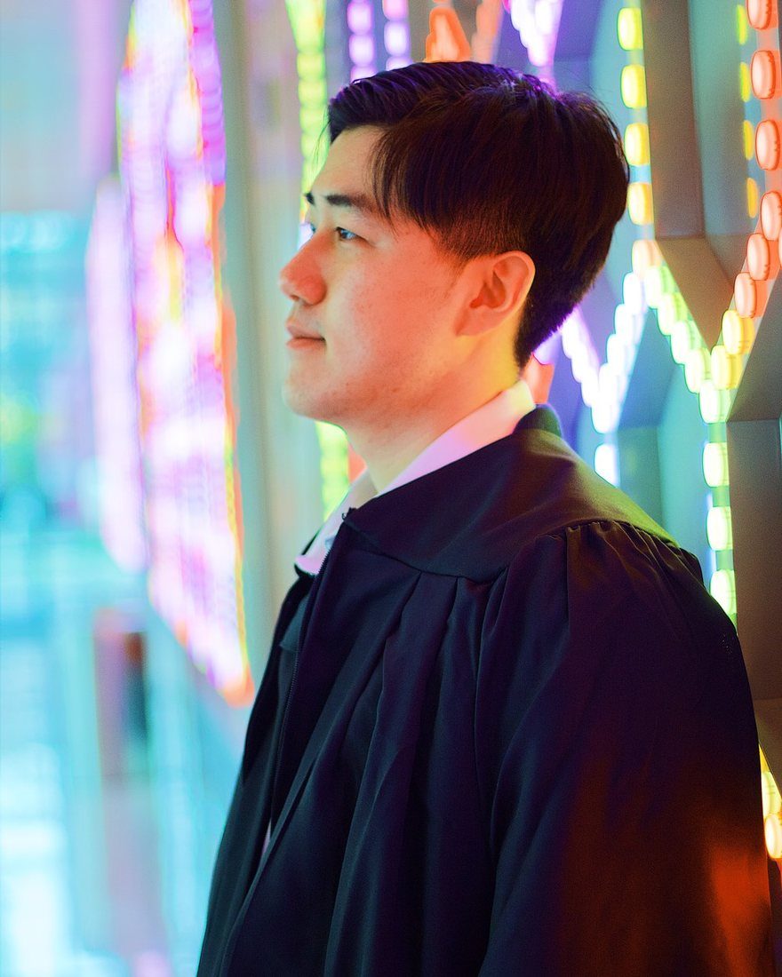 Profile portrait of a graduate in his gown, lit by a wall of colored lights